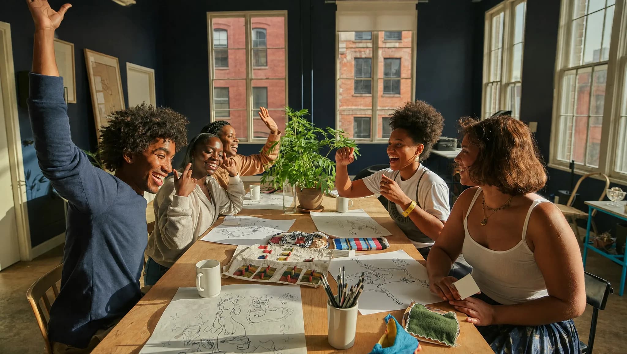 Young African creators celebrating together around a table of sketches and fabrics